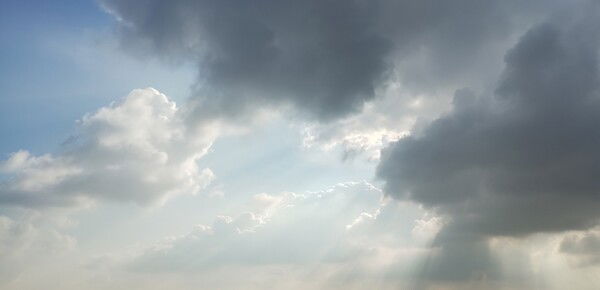 Picture of the sky. Half of the sky is full of darker clouds, while the other half has sunlight leaking through the dark clouds, illuminating the other half.