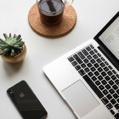A cactus, a cup of coffee, a phone and a laptop on a white table