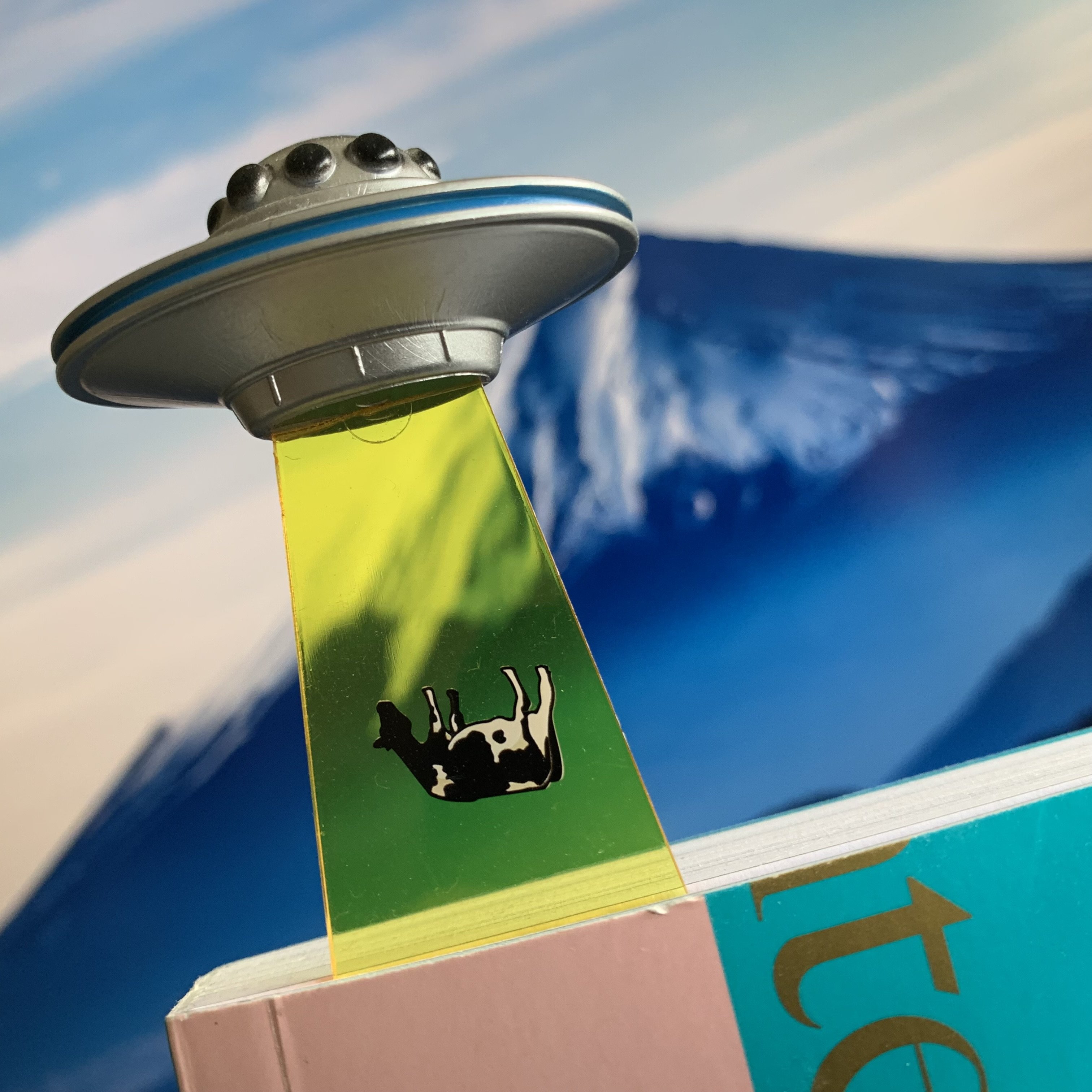 UFO Bookmark showing a cow being beamed up into a craft. Image of Mt Fuji in background. 