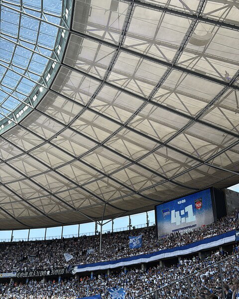 A football stadium scoreboard displays the score 4:1 under a partially covered roof.
Ein Fußballstadion-Anzeigetafel zeigt die Punktzahl 4:1 unter einem teilweise bedeckten Dach.