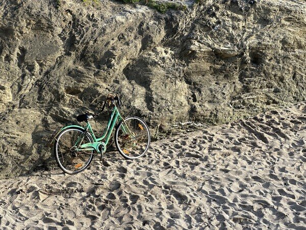 An old, rusty bicycle leaning against a rock wall on a beach.