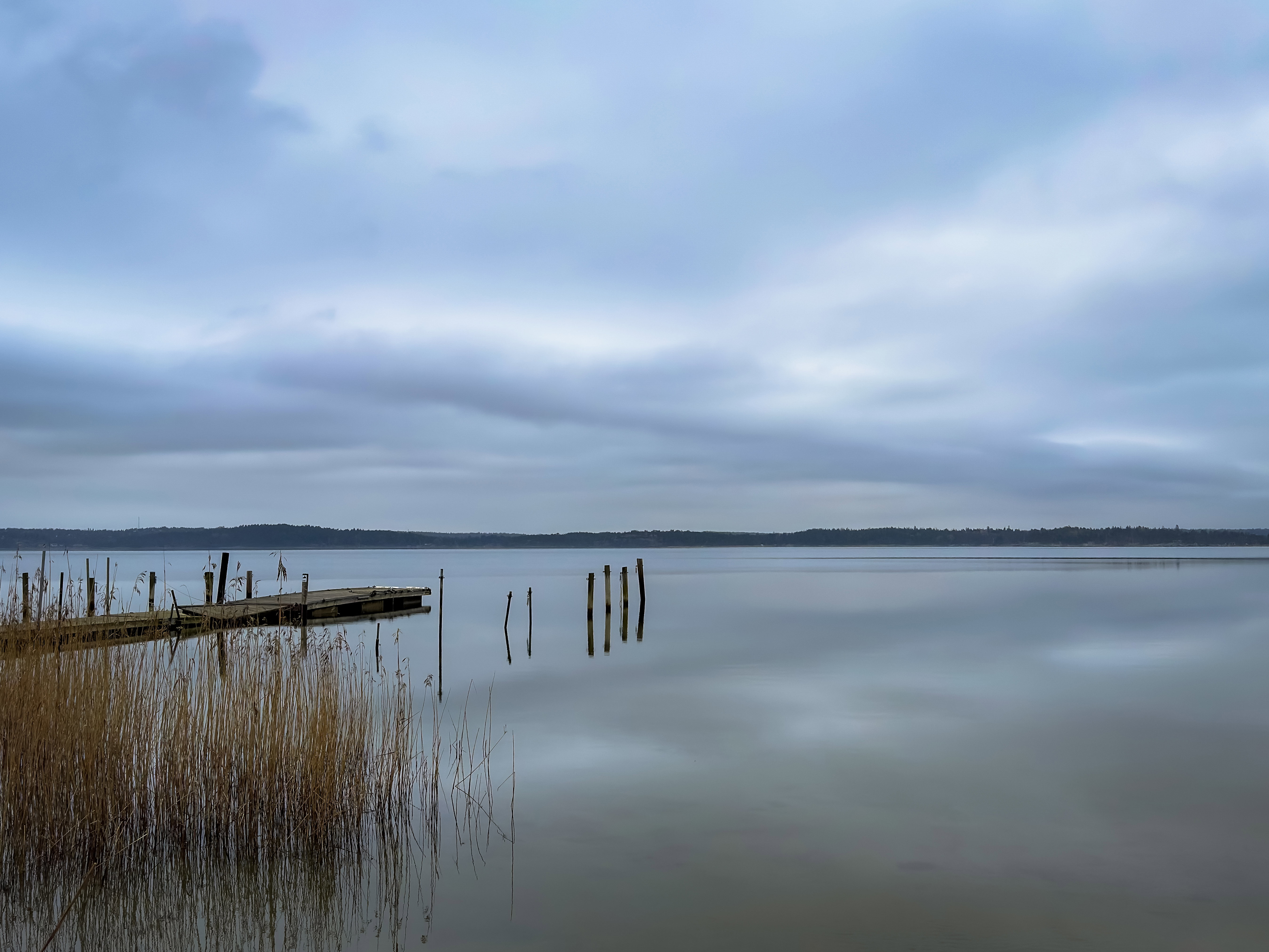 A mirror-still lake reflecting the soft blue-grey clouds.