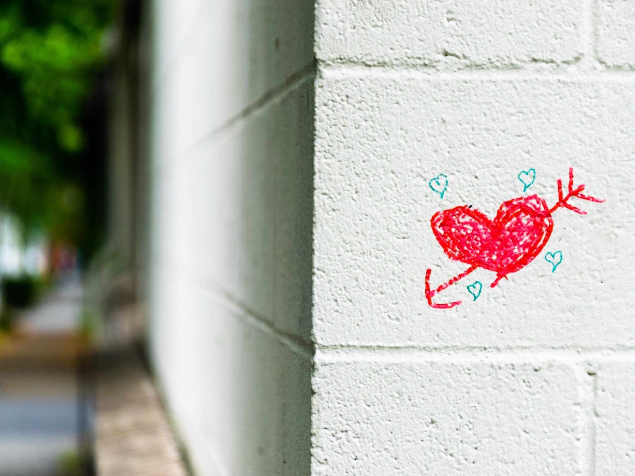 A red graffiti heart with smaller blue graffiti hearts around it, on the right side of the frame with the sidewalk out of focus on the left.