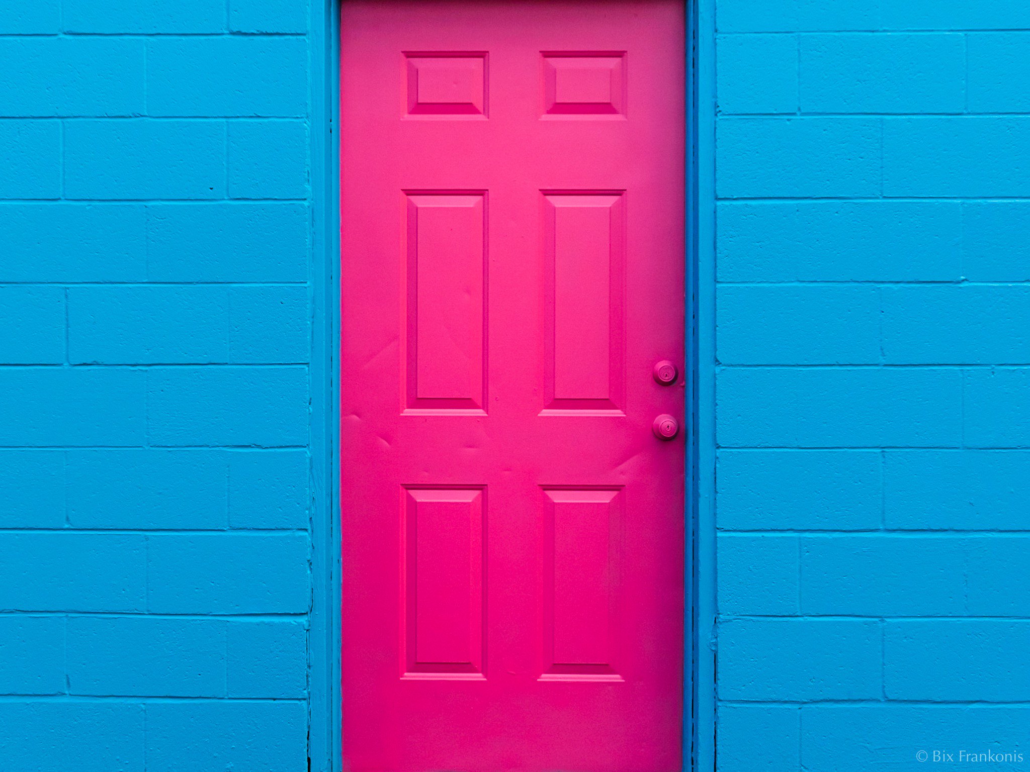 A pink door in a blue cinderblock wall.