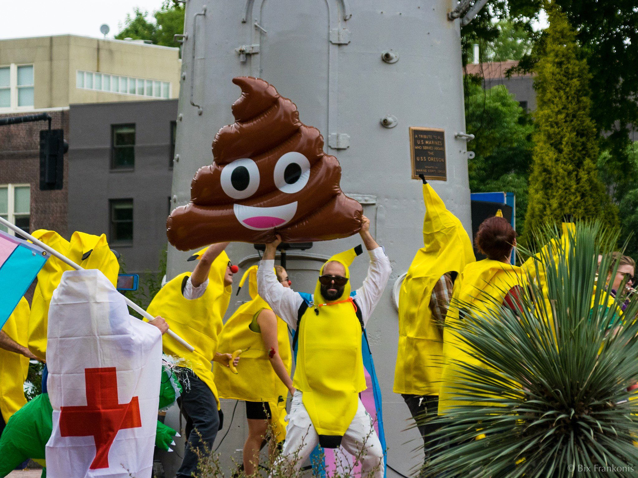 A man in a banana costume turns from a line of people in banana costumes to hold up a giant poop emoji