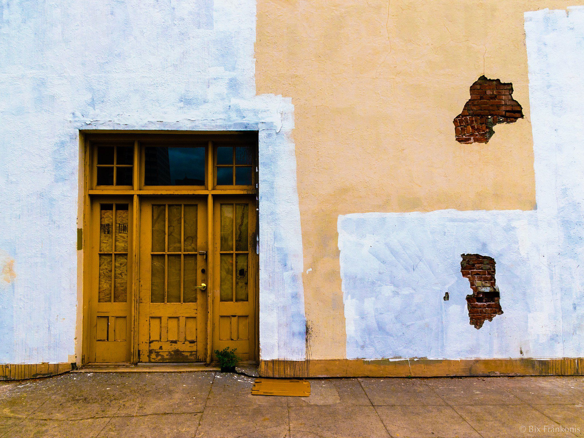 A wall with brick showing through holes in the facade and a wood-framed entry.