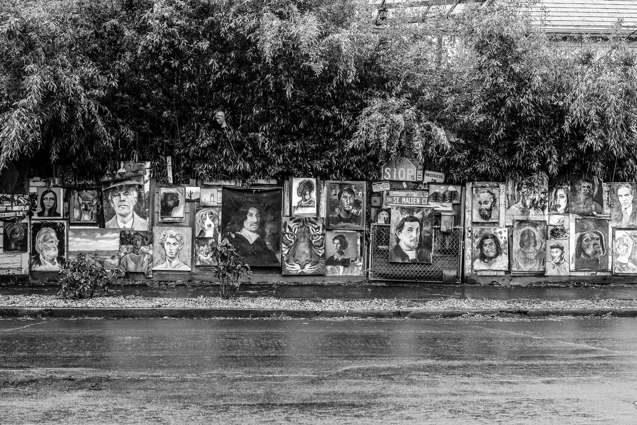 The outside of a fence completely covered by paintings of many different types, in black-and-white