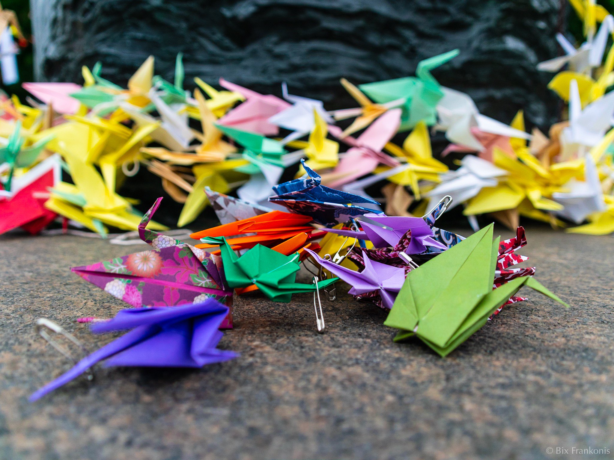 A small pile of paper cranes in focus in front of a larger pile in behind and out of focus.