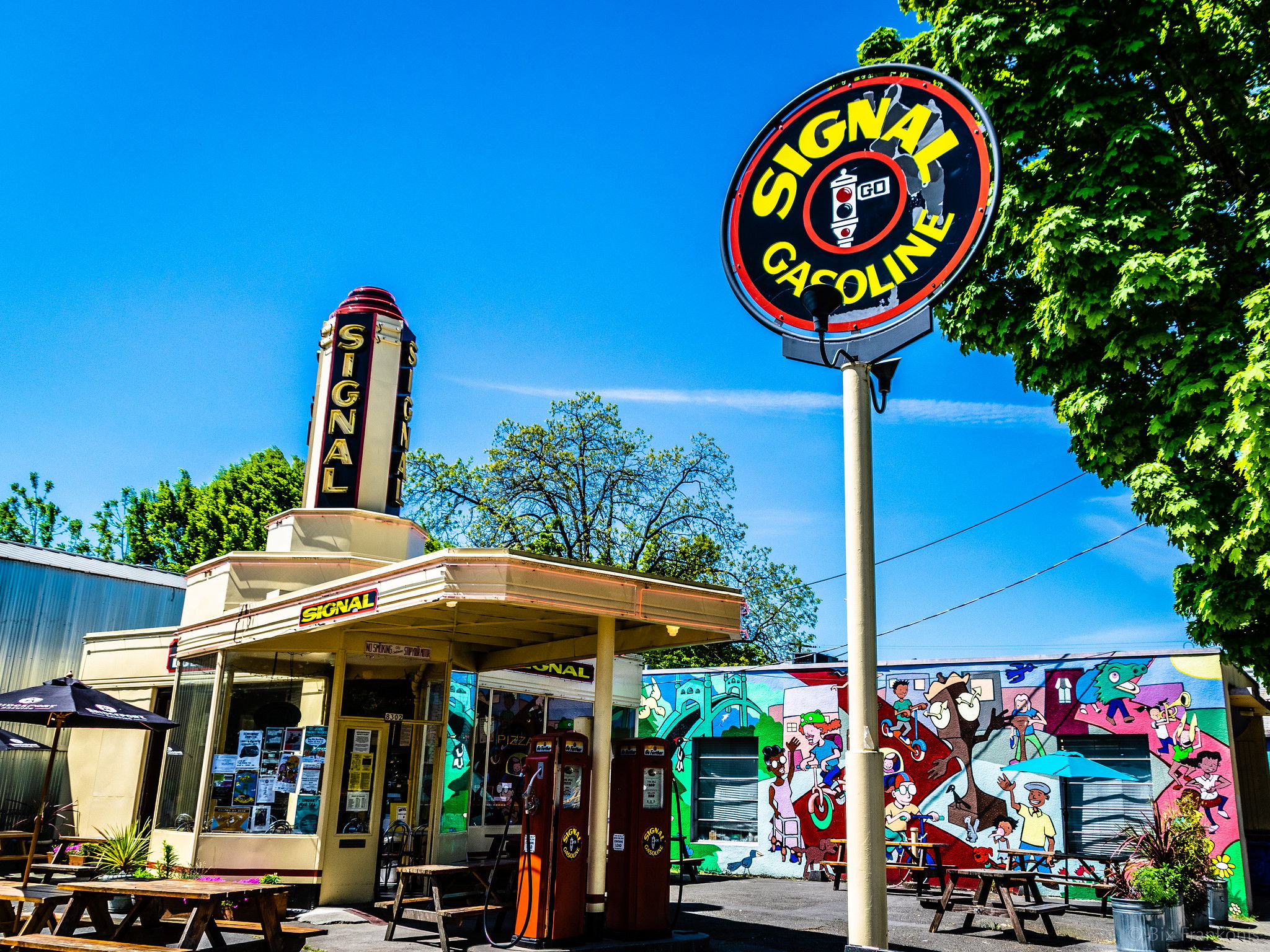 Wide angle on a vintage yellow gas station under blue skies with a tall sign still reading Signal Gasoline.