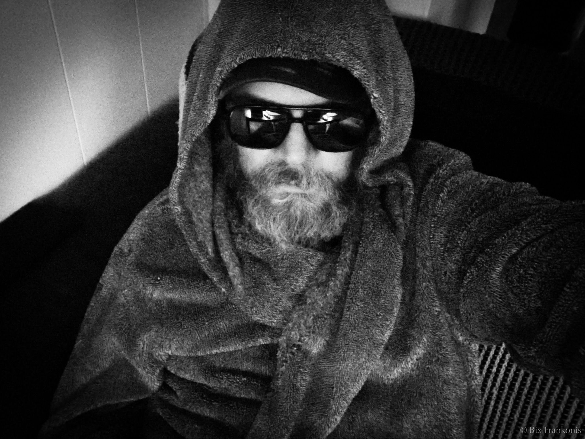 A middle-aged man sitting in the dark, in mirrorshades and hooed bathrobe.