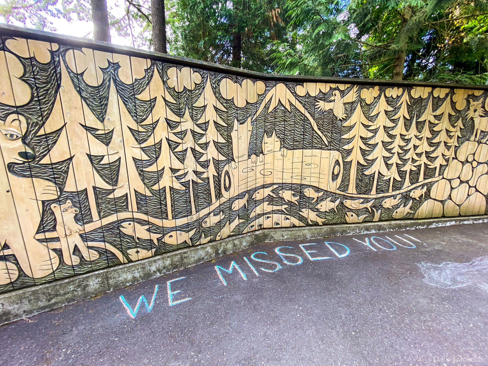 Below a carved wall of a forest scene is written in chalk “WE MISSED YOU!”