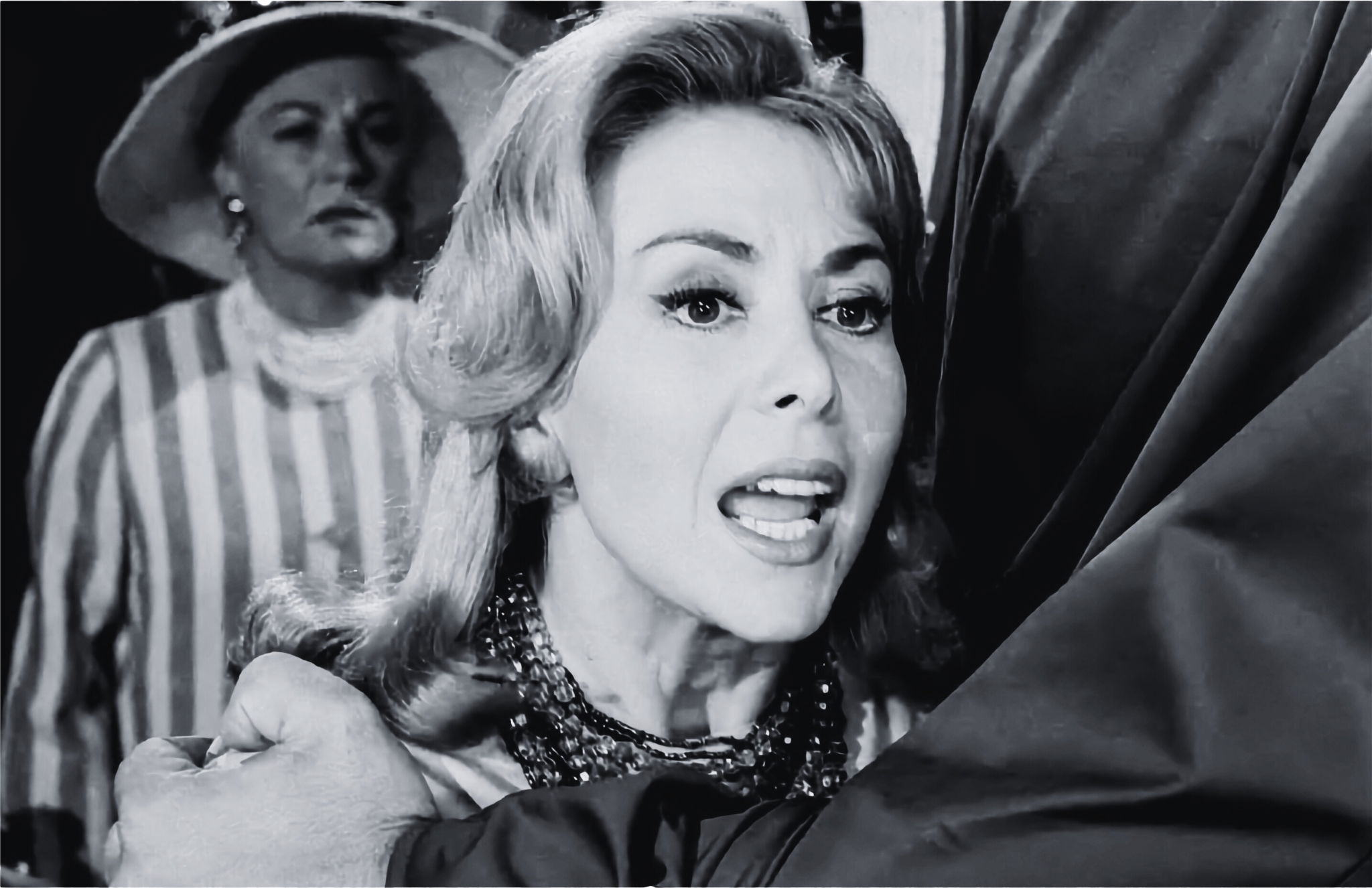 A blonde white woman, being held back by someone’s arm, is yelling.