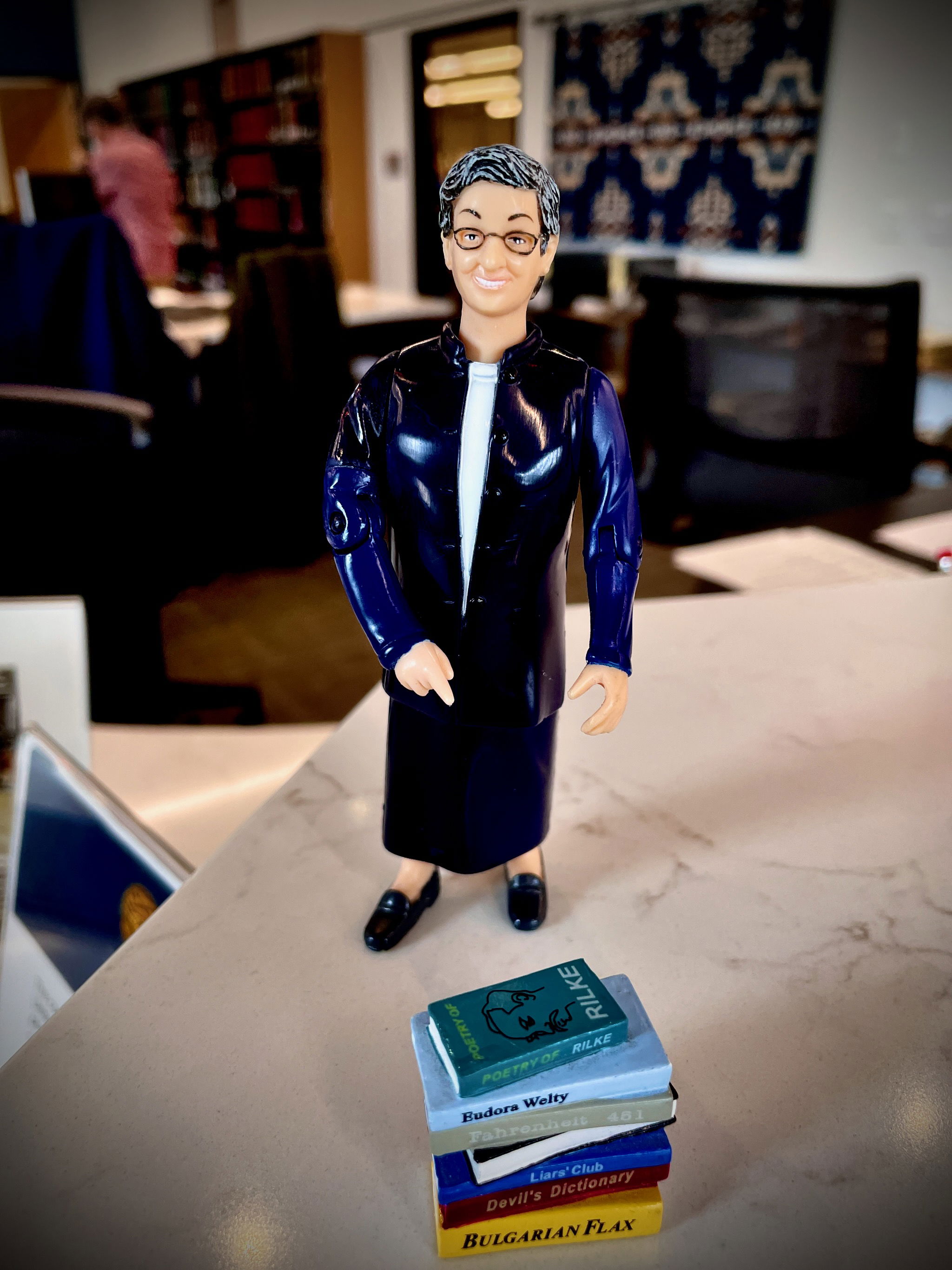 Close view of a tiny librarian figure with stack of tiny books, on a counter.
