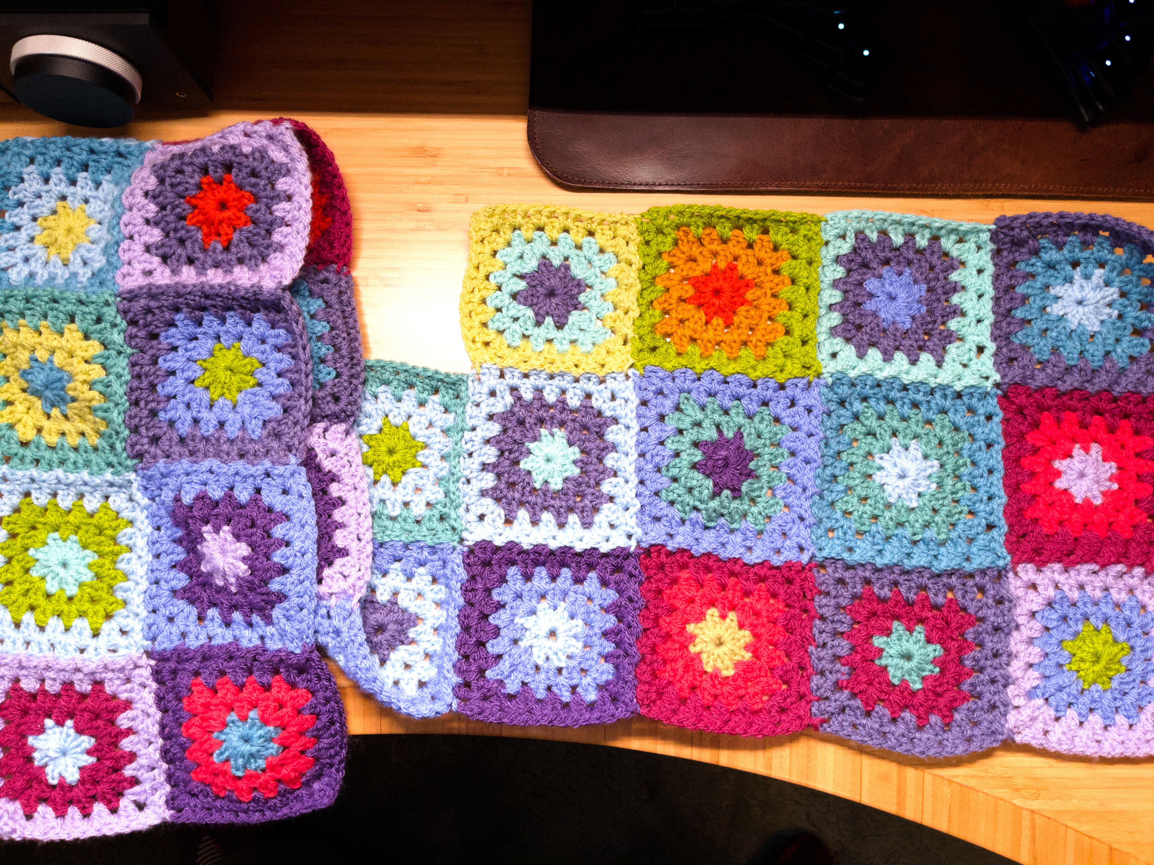 Two and a half rows of crocheted granny squares forming the start of a blanket. Each square is made up of three colours.