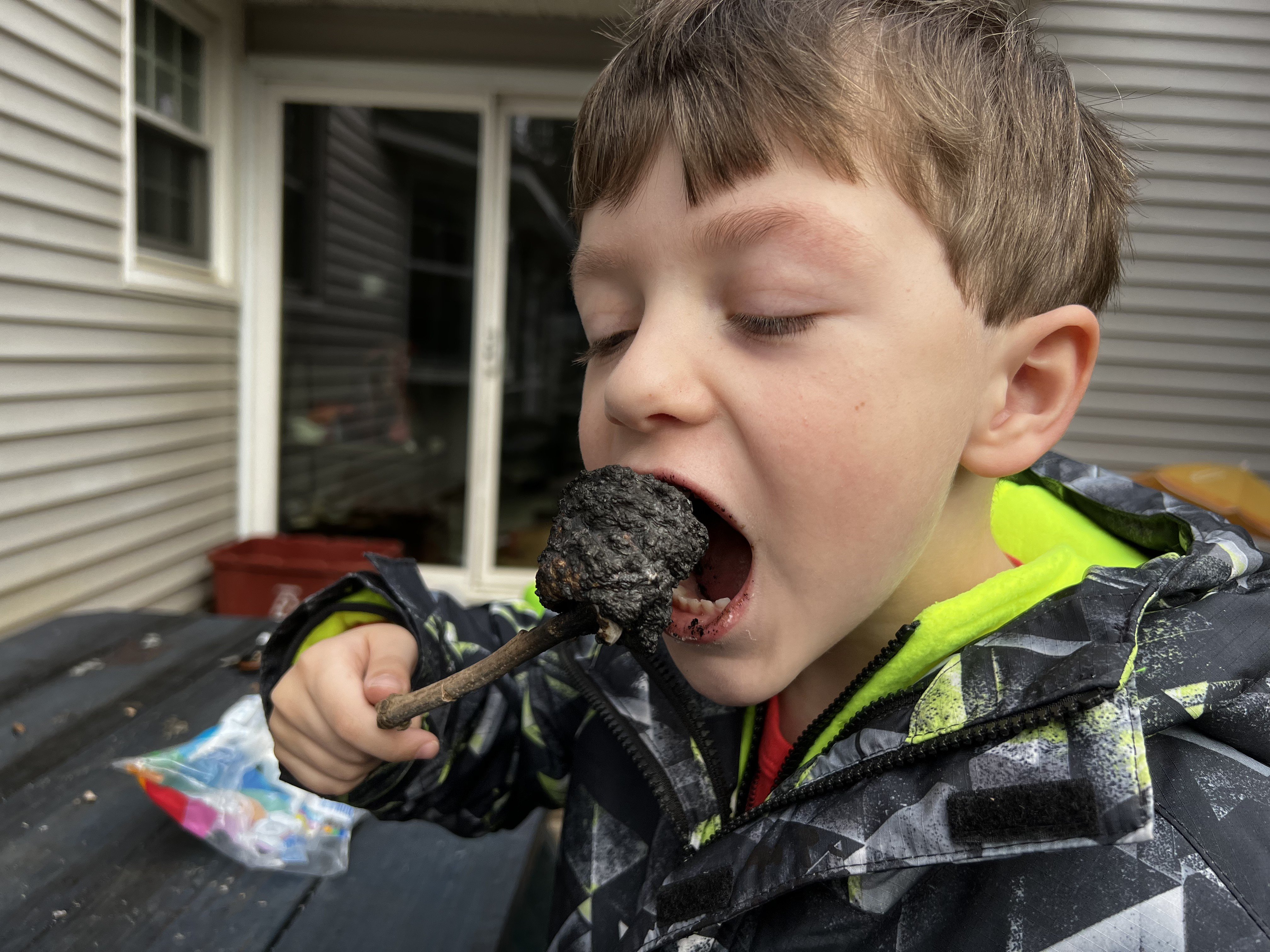 A boy eats a (burnt) toasted marshmallow.