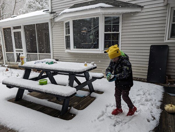 A boy makes a snowball while standing on a deck covered in snow. 