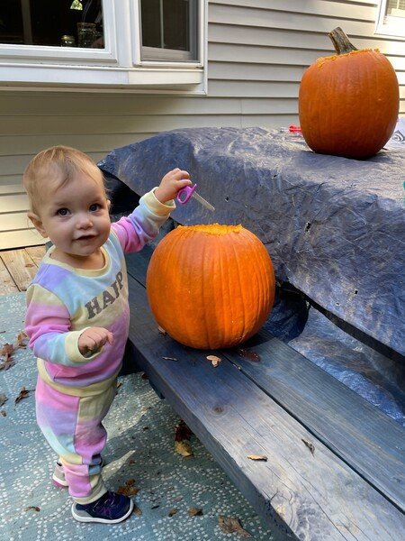 A small girl stands ready to carve into a pumpkin.