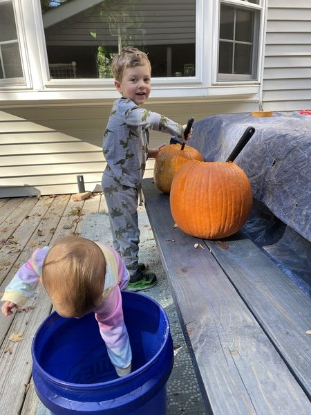 A boy stands carving a pumpkin, which is placed on the bench of a picnic table