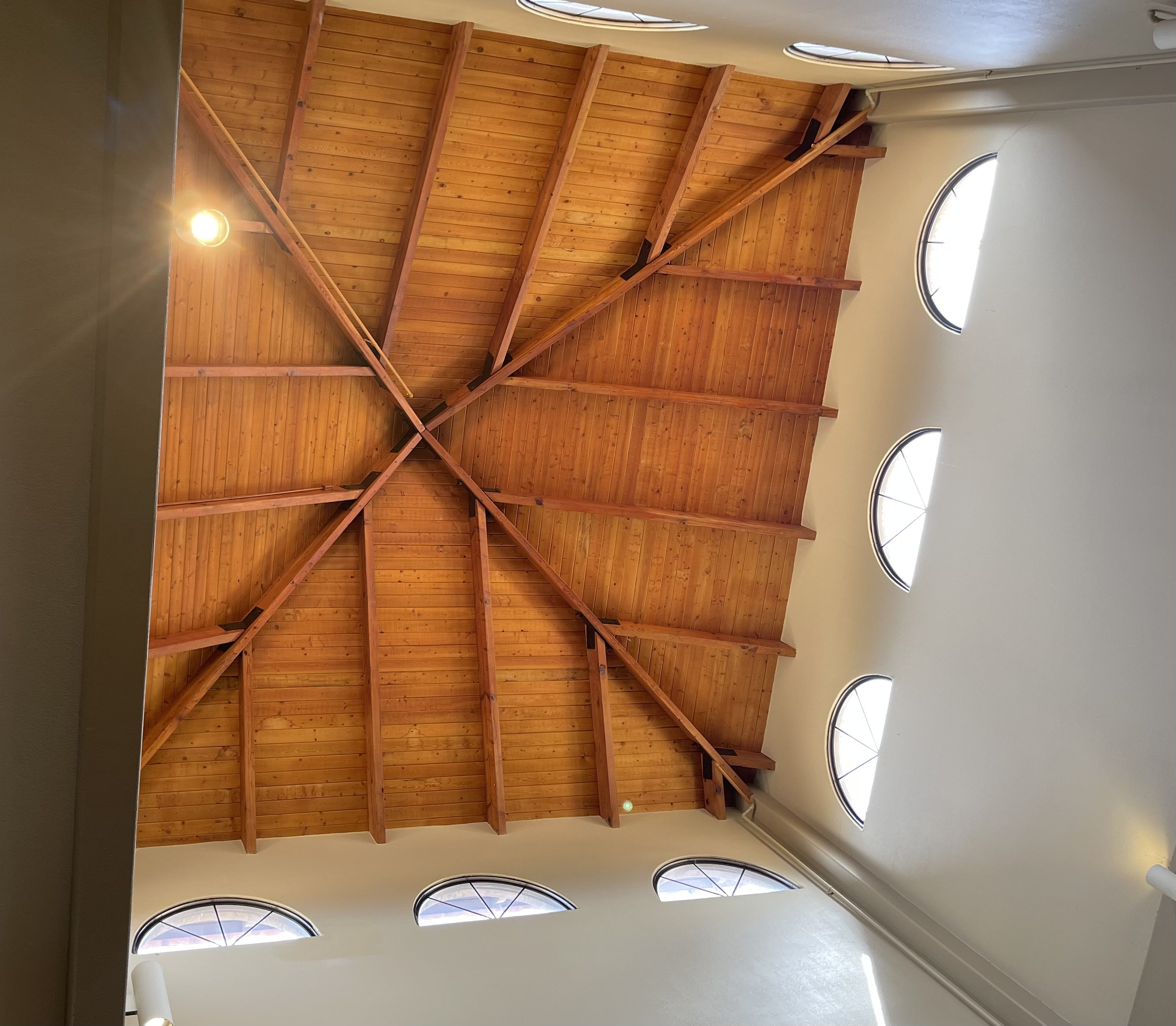 Interior view from below of a high peaked roof constructed of wood framing and planks. 