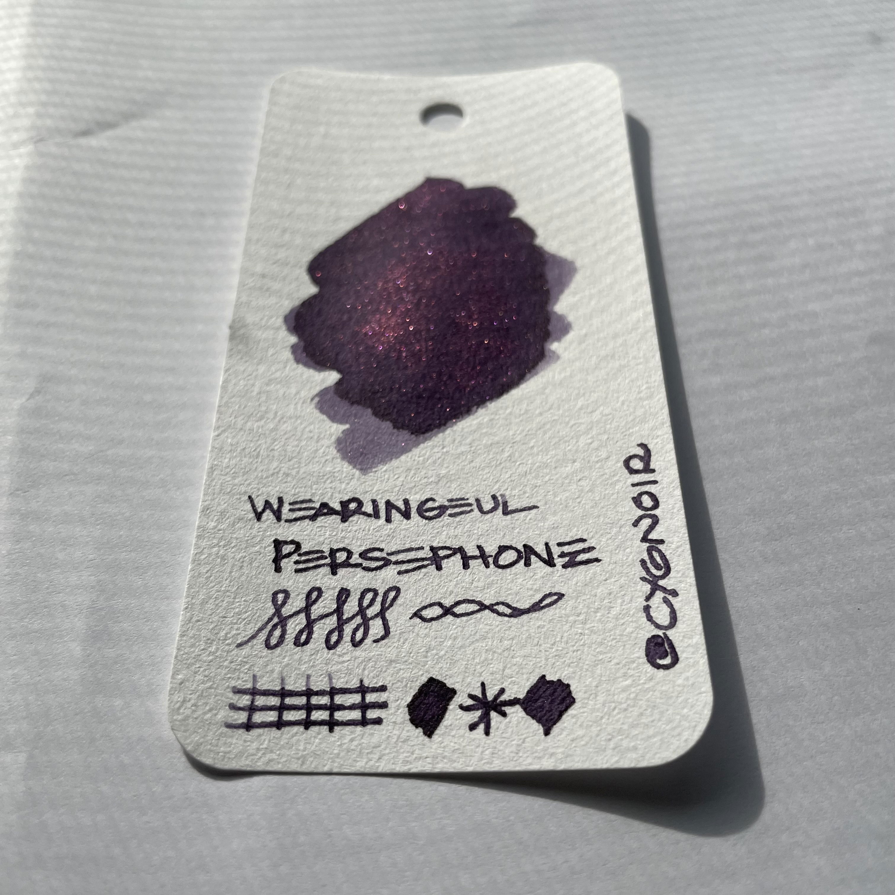 a swatch of Wearingeul Persephone fountain pen ink, dark violet ink with red shimmer on a white card.
