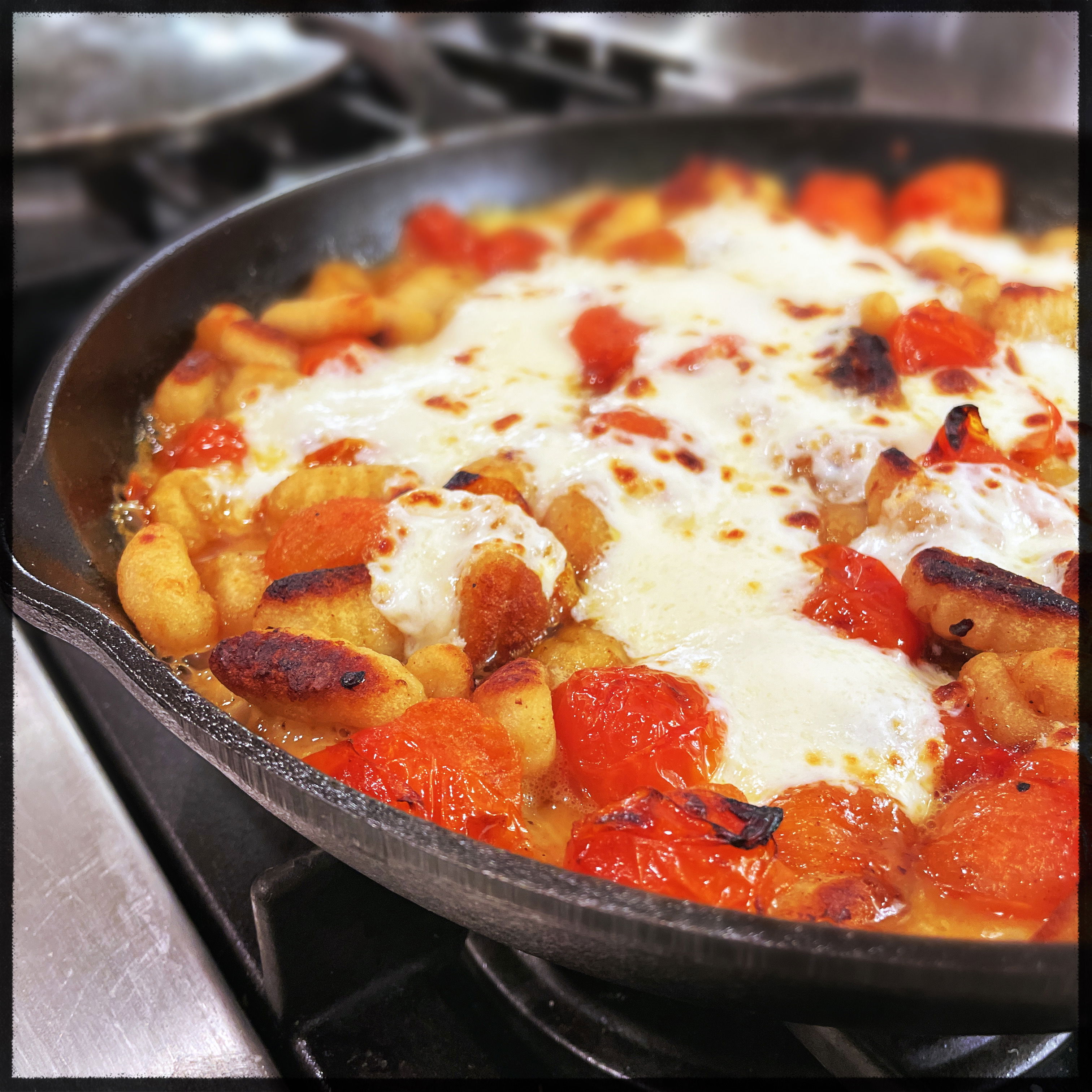 closeup of a cast-iron skillet with browned gnocchi, burst cherry tomatoes, and a river of melted mozzarella