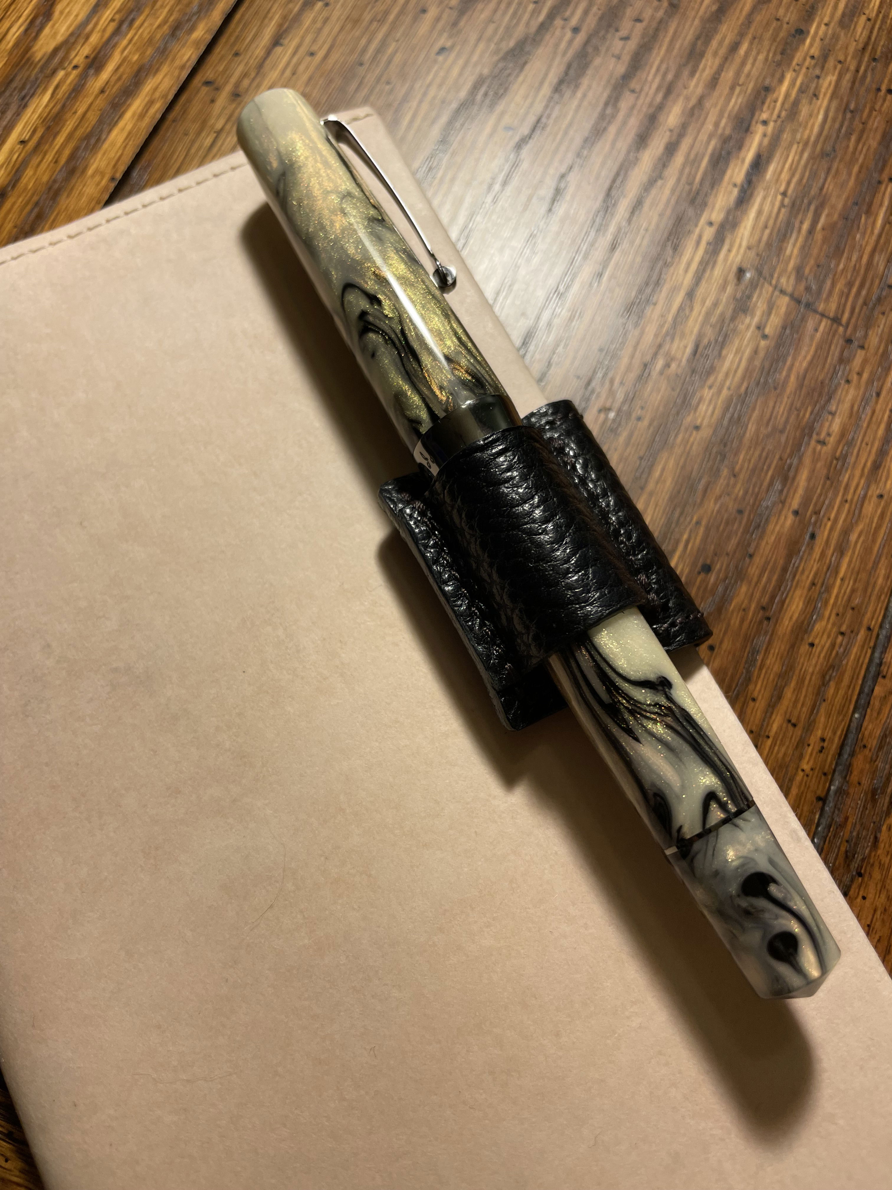 a fountain pen with cream, golden, and black swirled resin in a black pen loop atop a cream notebook