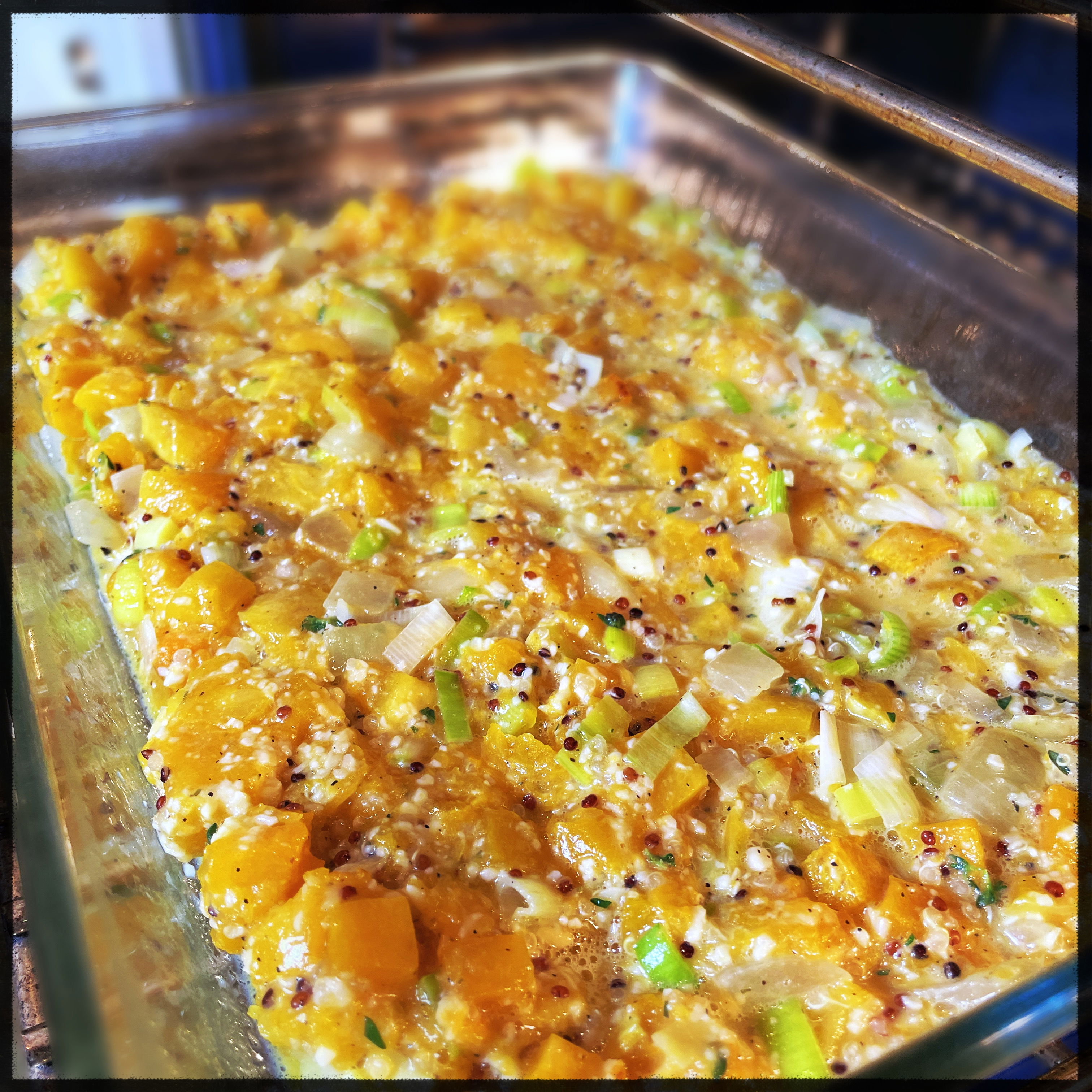 closeup of a glass baking dish that appears to contain cubed butternut squash, chopped leeks, and quinoa, before it has been baked