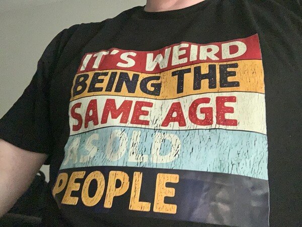 A black t-shirt with an inscription saying “It’s weird being the same age as old people”.
