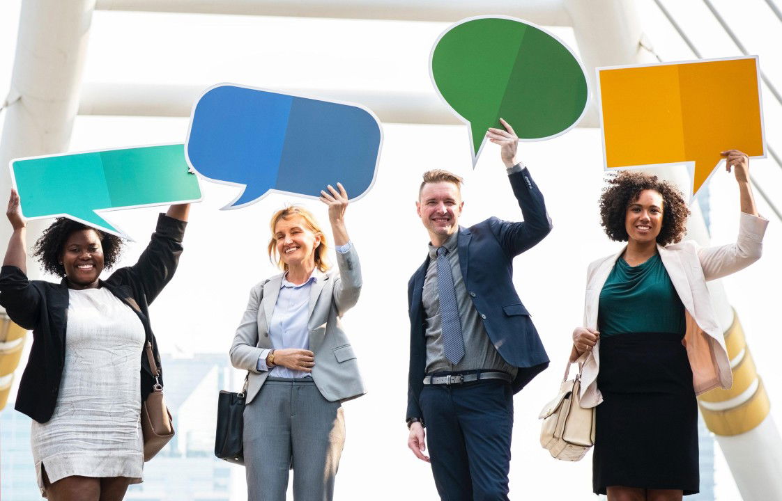 Stock image of four diverse proffessional people holding differently coloured and differently shaped speech bubble cards
