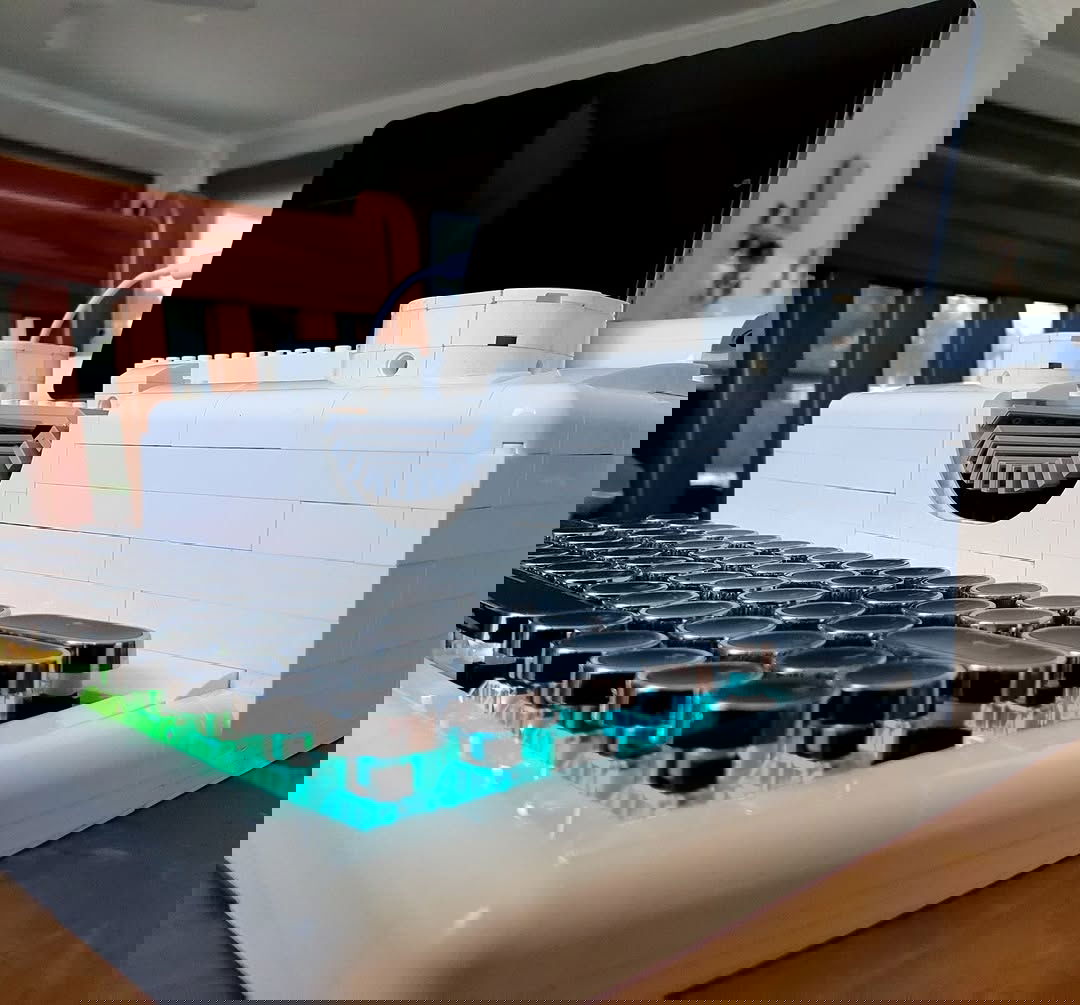 A front-left shot of a white, Lego-built typewriter with an RGB mechanical keyboard for the keys. The keys have rounded keycaps. There is a tablet sitting on top as if it was the paper and is plugged in via USB.