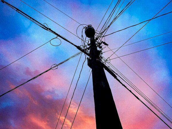 Silhouette of a utility pole and wires against a colorful sky.