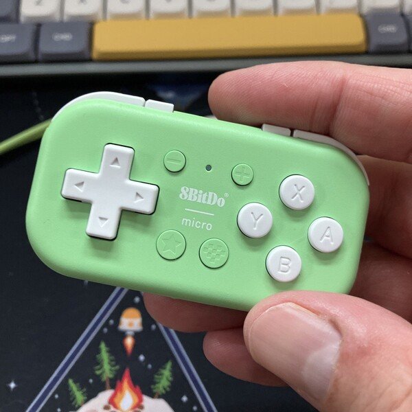 Ein hellgrünes, sehr kleines Gamepad, das mit Daumen und Zeigefinger in die Kamera gehalten wird.
