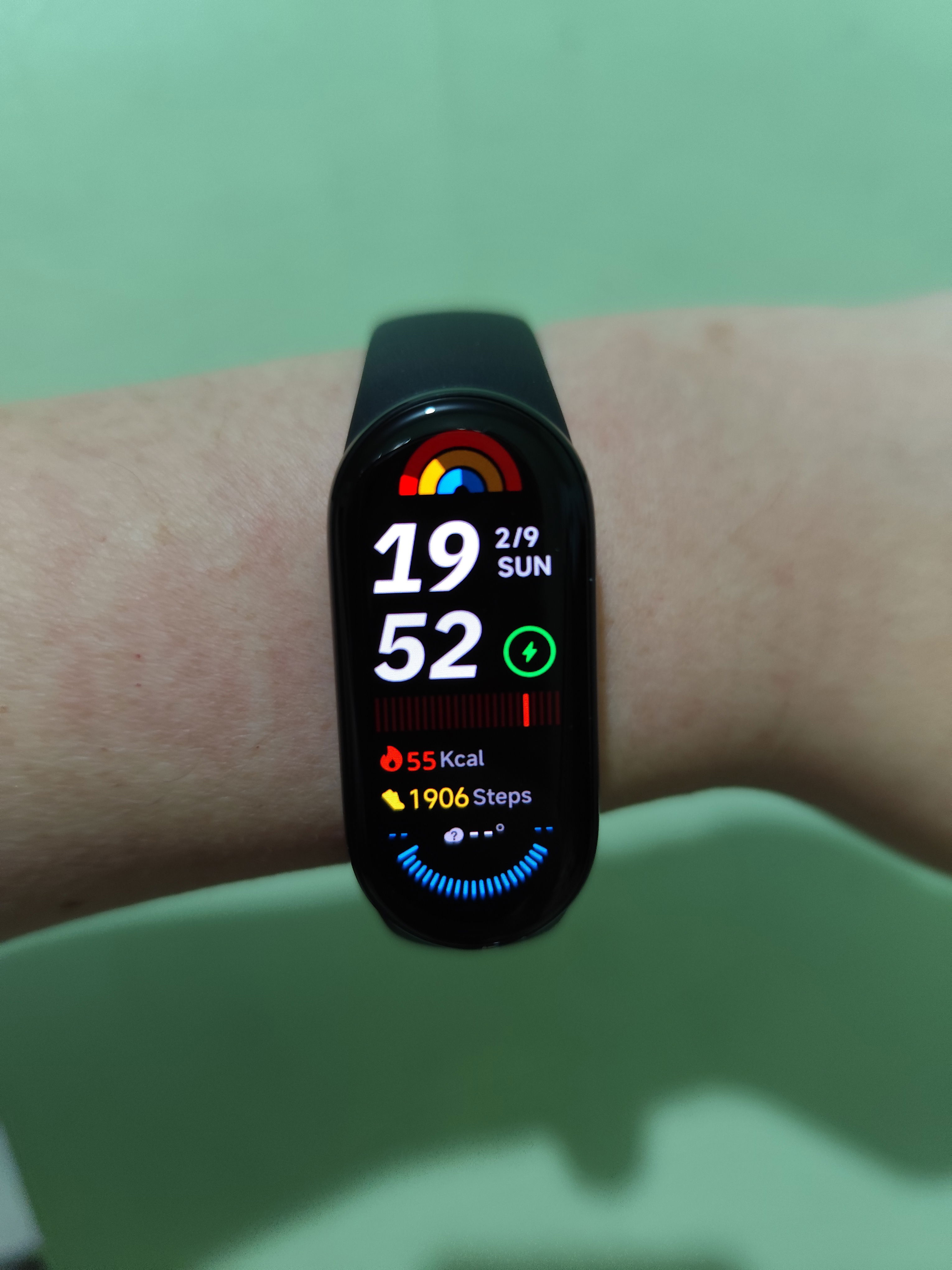 Close-up photo of my left wrist wearing a black Xiaomi Smart Band 9 smartwatch, with the screen on and displaying information about time, date and health.