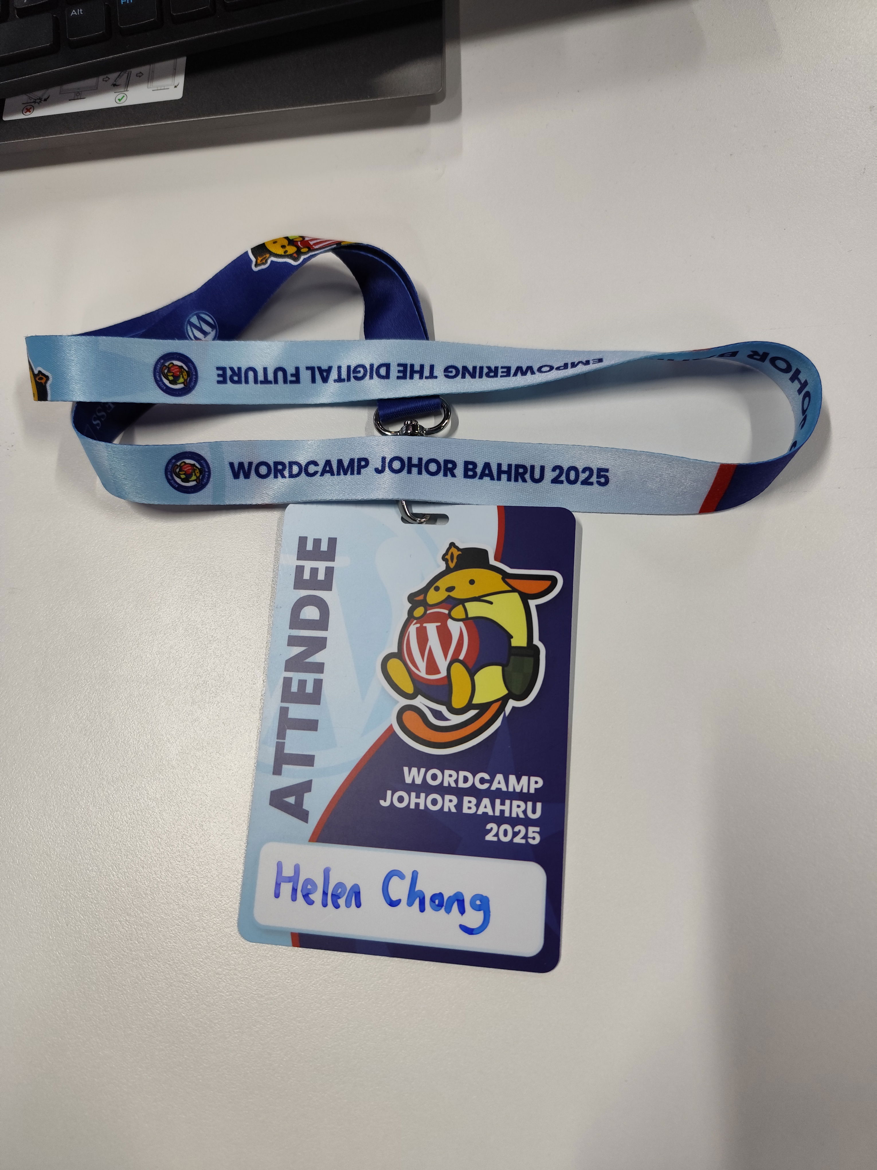 Photo of an attendee card of WordCamp Johor Bahru 2025, written with the name Helen Chong and printed with Johor version of Wapuu, the WordPress mascot.