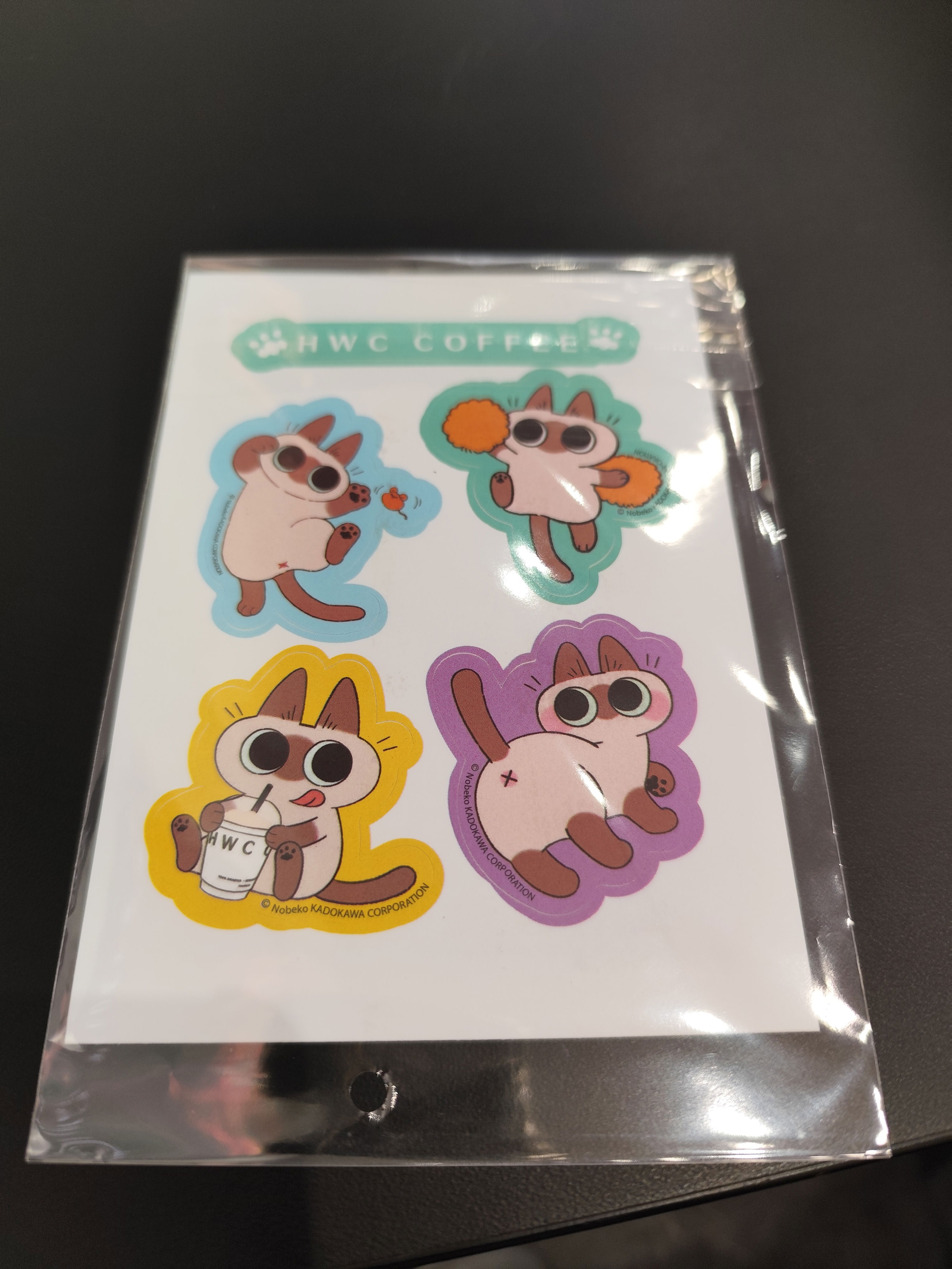 Four stickers of the cream-coloured cat mascot of HWC Coffee in different poses, including playing with a mouse, cheerleading, drinking a cup of HWC Coffee, and showing its backside.
