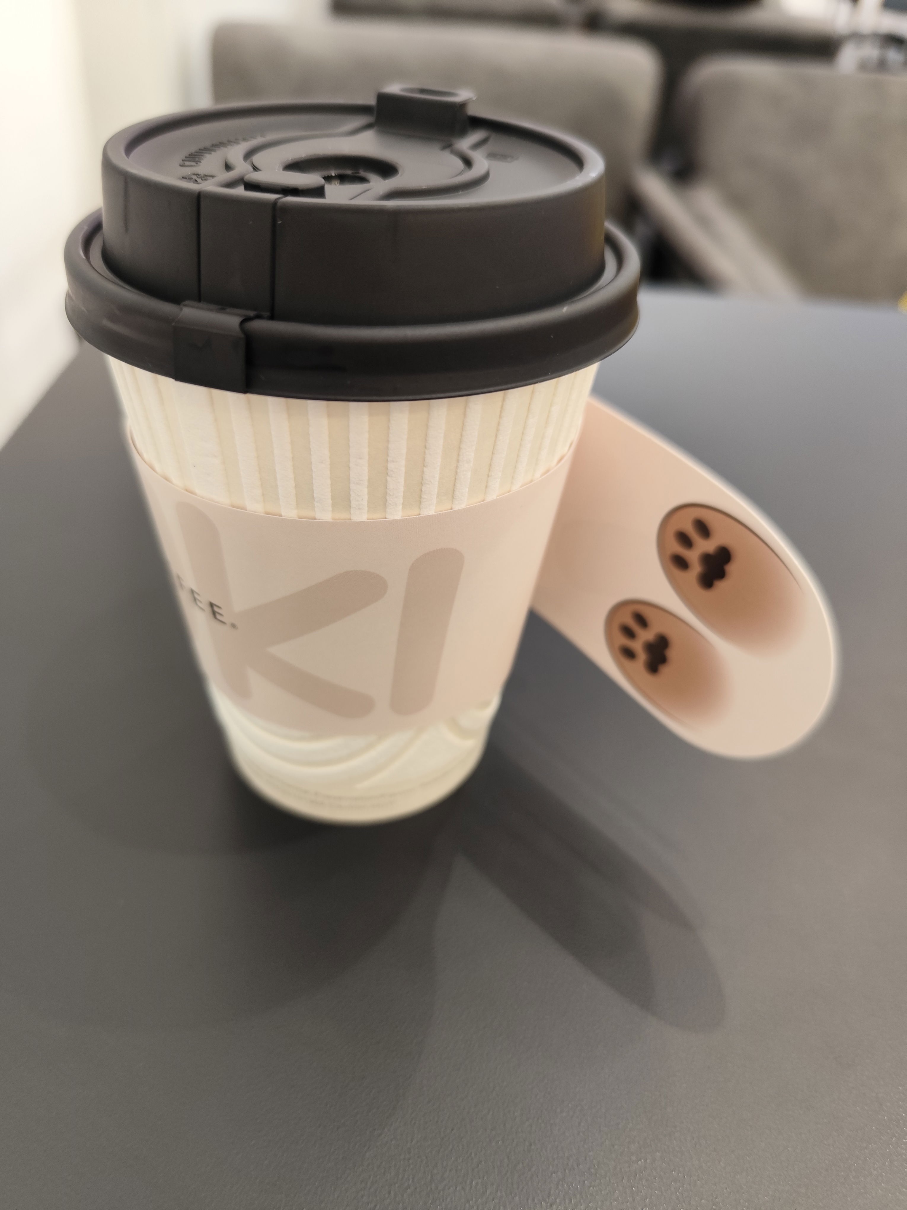 Coffee cup of HWC Coffee, with the cup sleeve designed with a cream-coloured cat mascot, with the camera shows the cat mascot's back legs.