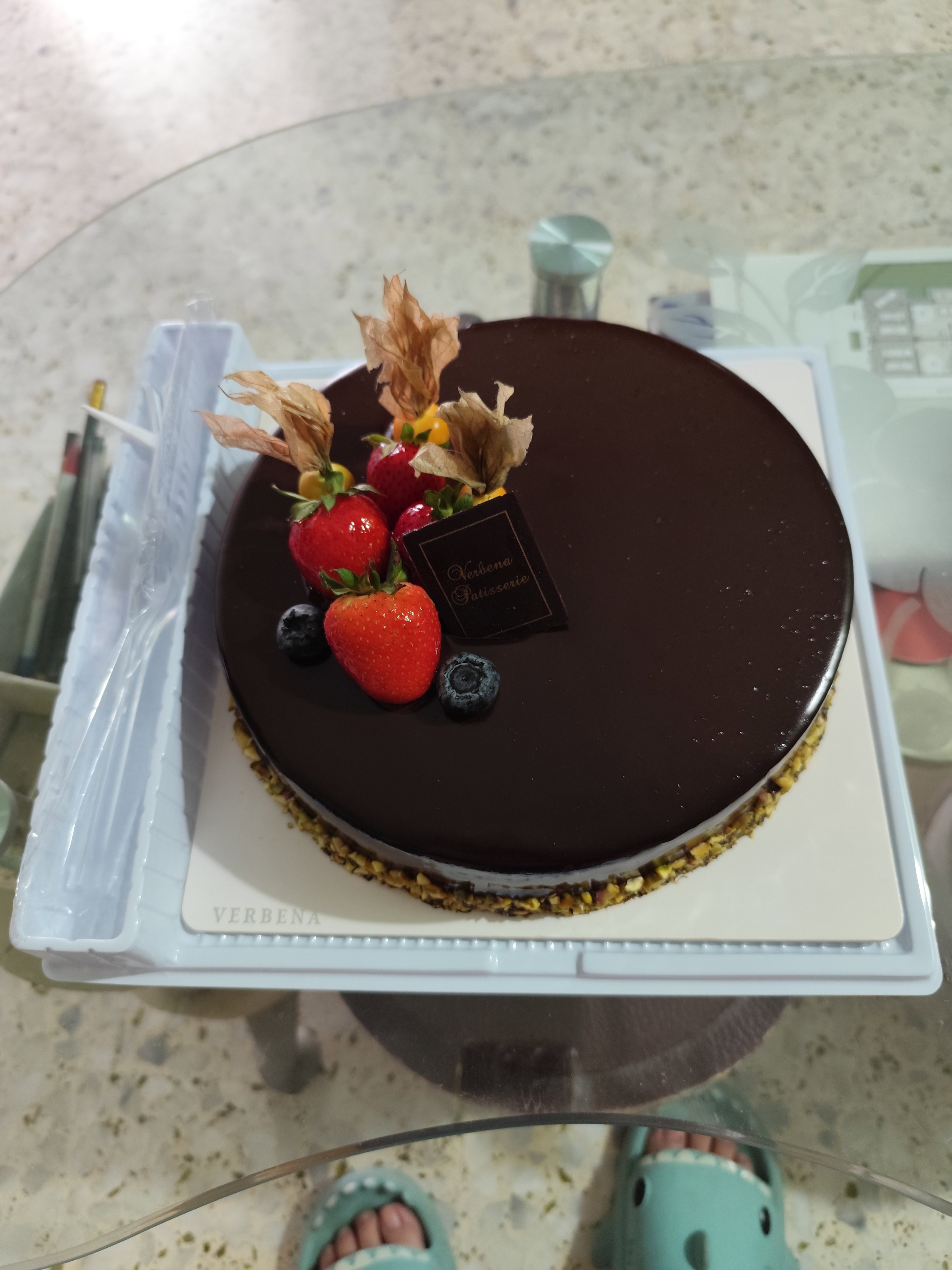 Photo of a chocolate mousse cake, with strawberries, blueberries and fake leaves on top of the cake.