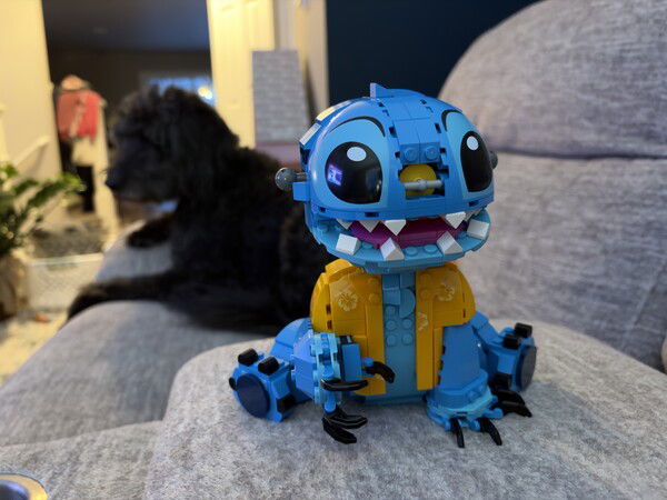 Nightmare fuel

Blue LEGO Stitch with big eyes and yellow chest sits on a gray couch next to a black dog.