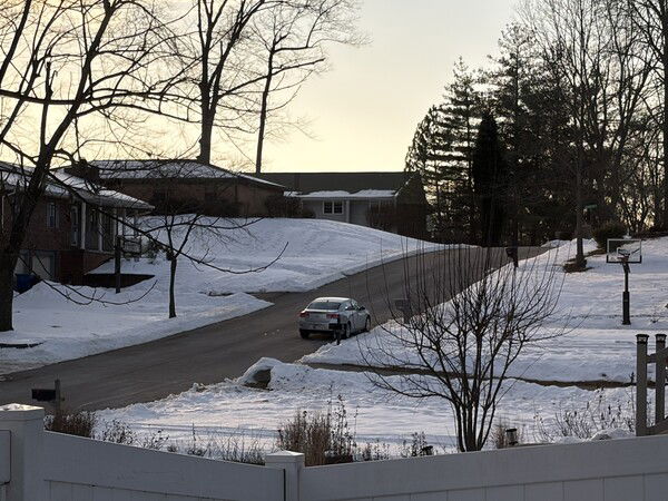 I like the streets clear but the snow still on the grass.

A car drives down a snowy street lined with houses and trees under a pale sky.