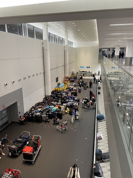 A wide angle of the baggage hall at Toronto Pearson Airport with suitcases stacked up by the dozens.