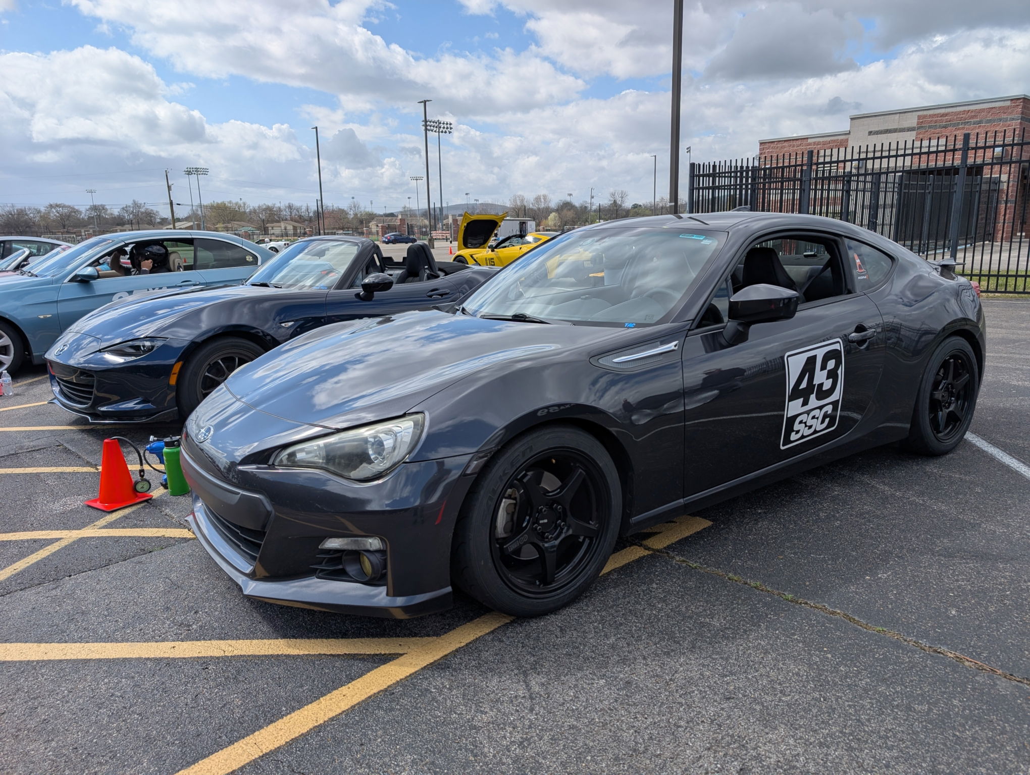 A dark grey sports car with 43 SSC on the side lined up next to some other sporty cars in a parking lot. 