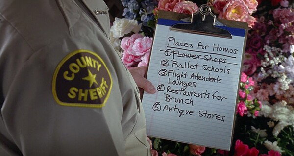 A scene from 'To Wong Foo Thanks For Everything Julie Newmar'. On a legal pad is a list titled 'Places for Homos' with the following items: flower shops (crossed out), ballet schools, flight attendants lounges, restaurants for brunch, antique stores.