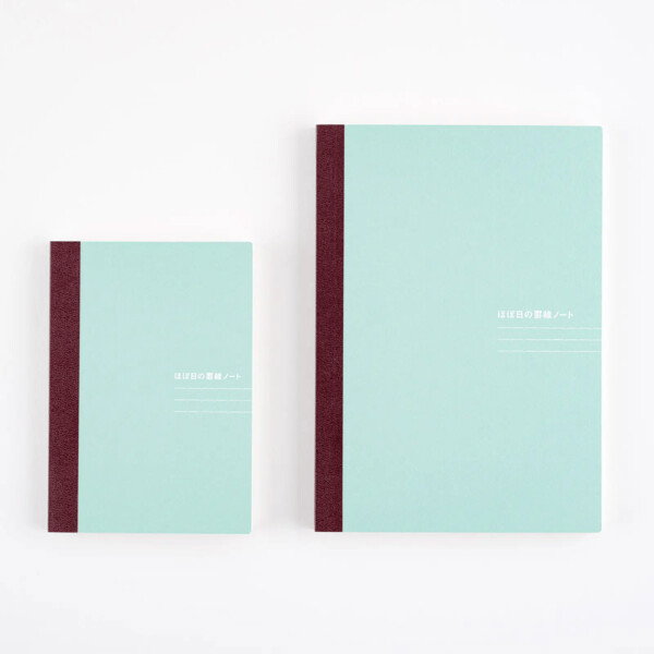 A product photograph showing two mint green notebooks with a dark red spine, placed side-by-side on a white surface. The notebook on the left is smaller and in a portrait orientation, while the one on the right is a larger version of the same design. Both notebooks have Japanese text on the cover, with the top line of text appearing slightly bolder. The image is a clean, minimalist studio shot with soft lighting, highlighting the product design.