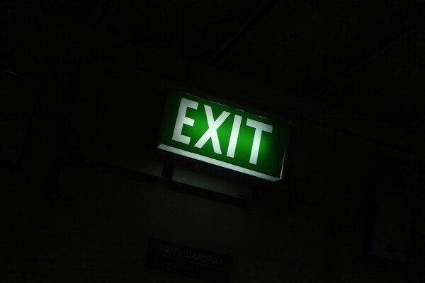 An illuminated green exit sign glows brightly against a dark, shadowy background, featuring the word 'EXIT' in bold, white capital letters. Below the main sign, a smaller, dimly lit plaque displays the Indonesian words 'PINTU DARURAT,' which translates to 'emergency door.' The image is captured with a high-contrast, low-key aesthetic, creating an atmospheric and slightly cinematic mood where the vibrant green light serves as the sole focal point in an otherwise pitch-black environment, emphasizing a sense of direction or safety within the darkness. Photo by [Auzan Zaky](https://unsplash.com/@slyzyy?utm_source=unsplash&utm_medium=referral&utm_content=creditCopyText) on [Unsplash](https://unsplash.com/photos/exit-signage-x0BeneG3lmc?utm_source=unsplash&utm_medium=referral&utm_content=creditCopyText)
      