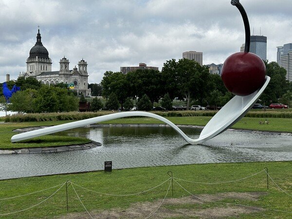 A large cherry on a spoon sculpture in a shallow pond of water.