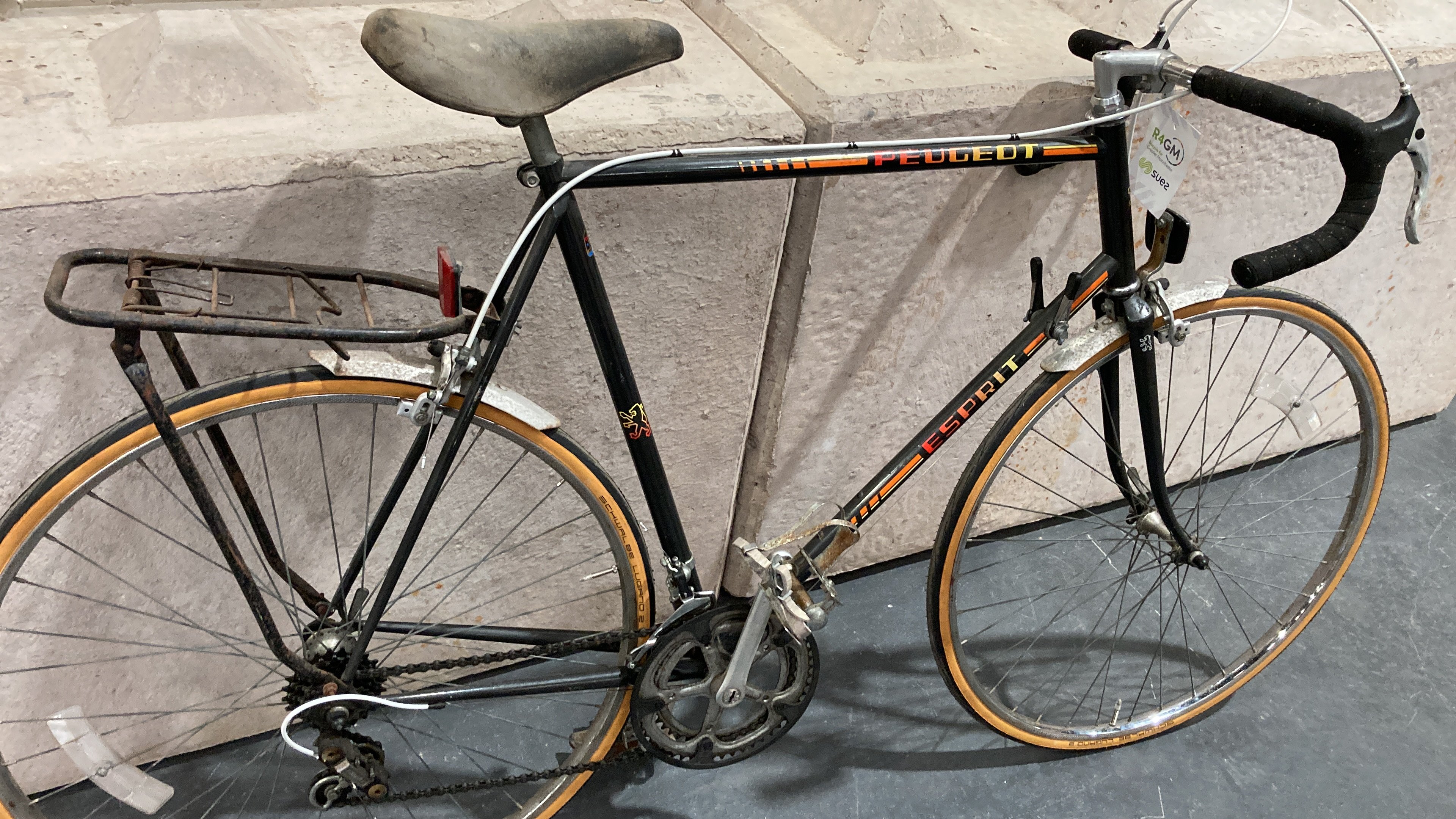 A well-worn Peugeot bike with black handlebars, a very faded saddle, and very 80's decals along the side.