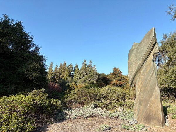 A modern carved slab-like statue stands against lush greenery.