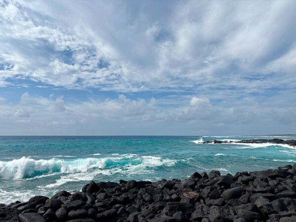 blue waves crash against black lava rocks 
