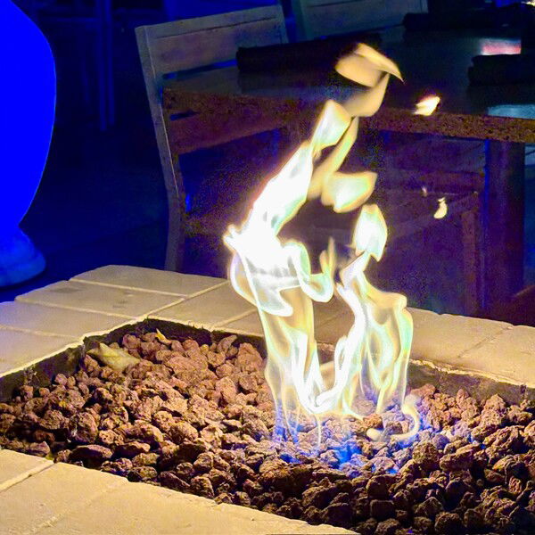 An orange gas flame dances above a fire pit with a blue light and granite table in the background.