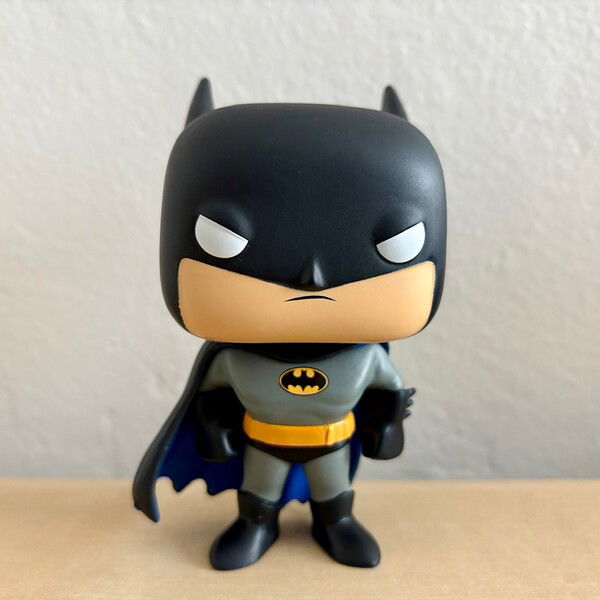 A Funko POP of Batman from Batman The Animated Series on a light wood table.